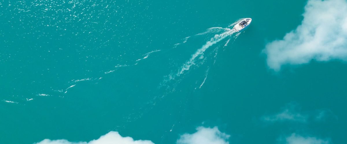 A motorboat glides across the stunning turquoise waters of Lake Attersee viewed from above.